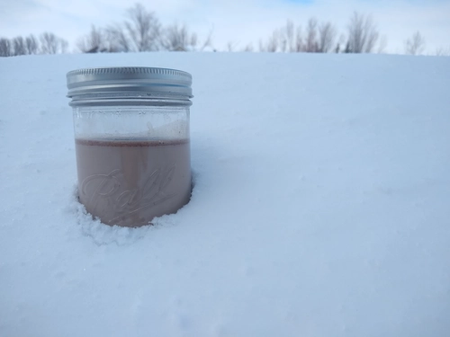 A jar of chocolate custard sitting in a snow bank